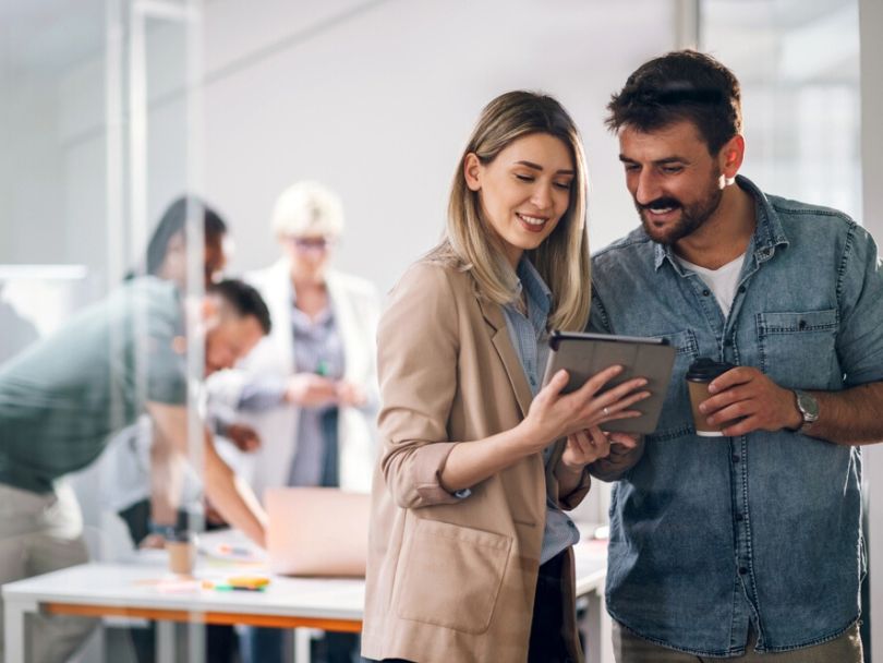 A professional woman and man look at data on a digital tablet while working together in an office